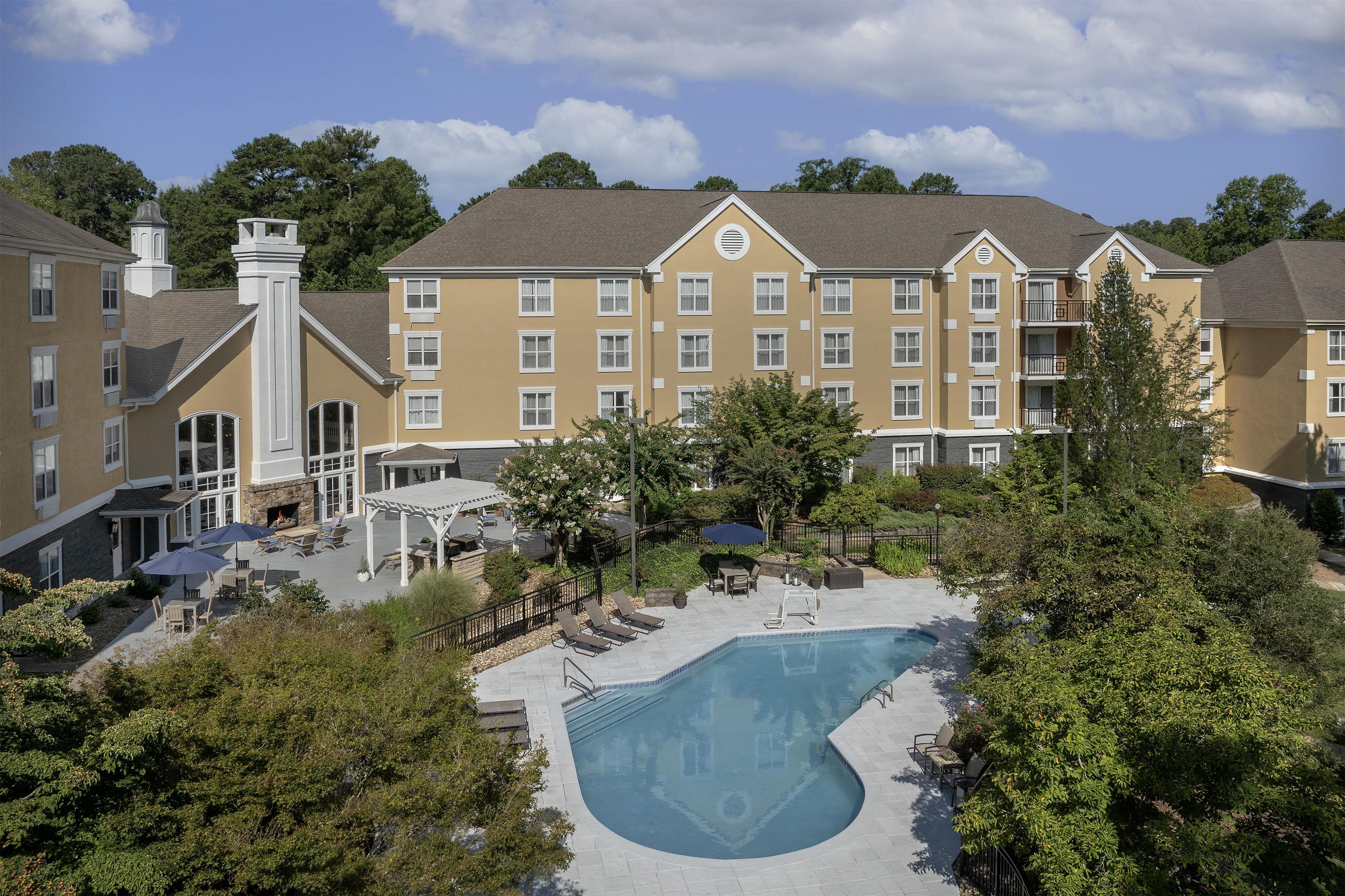 A hotel with a swimming pool, outdoor seating, and a covered patio area.