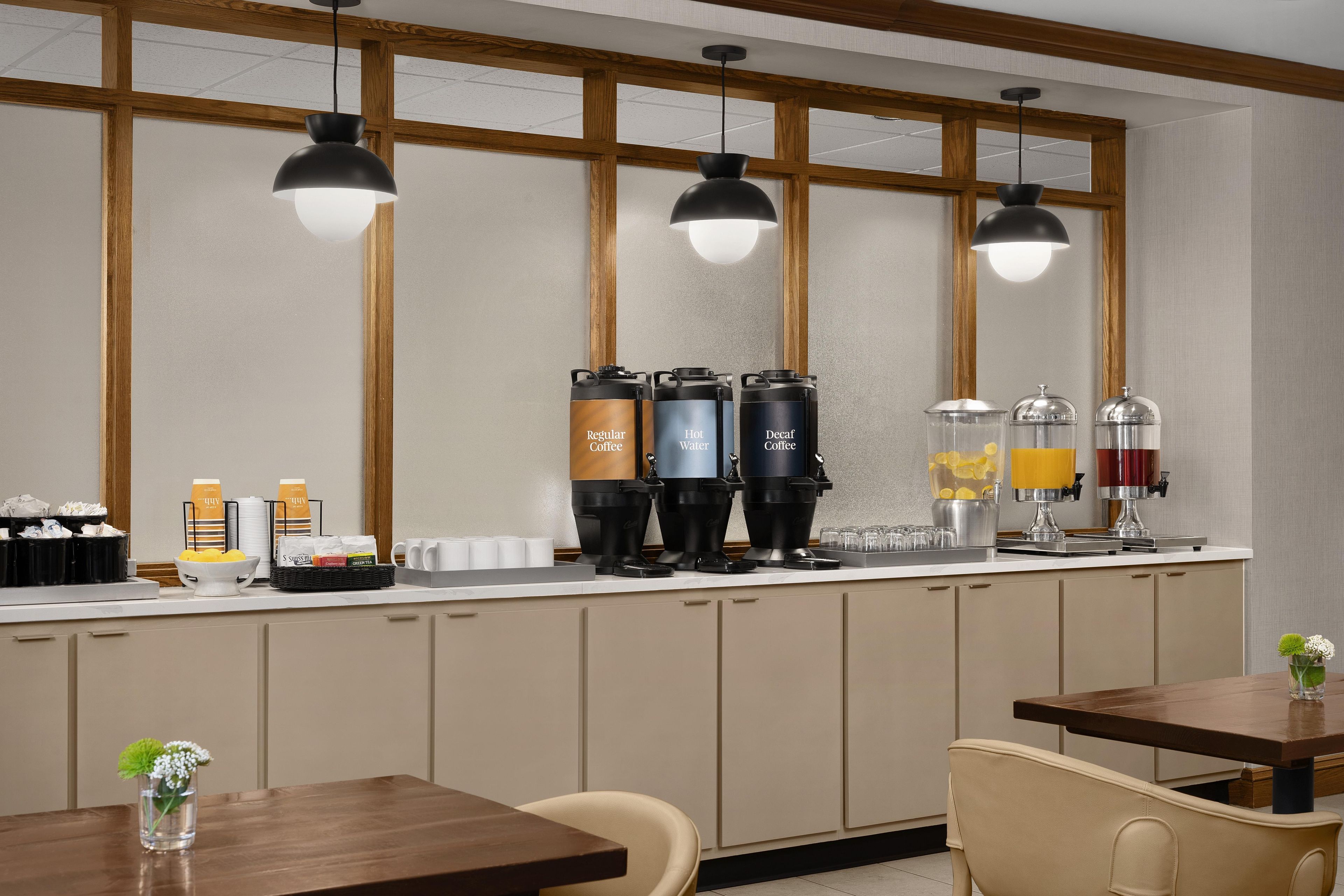 A modern kitchen with a bar area, equipped with coffee machines, a water dispenser, and a juice station.