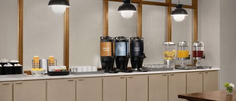 A modern kitchen with a bar area, equipped with coffee machines, a water dispenser, and a juice station.