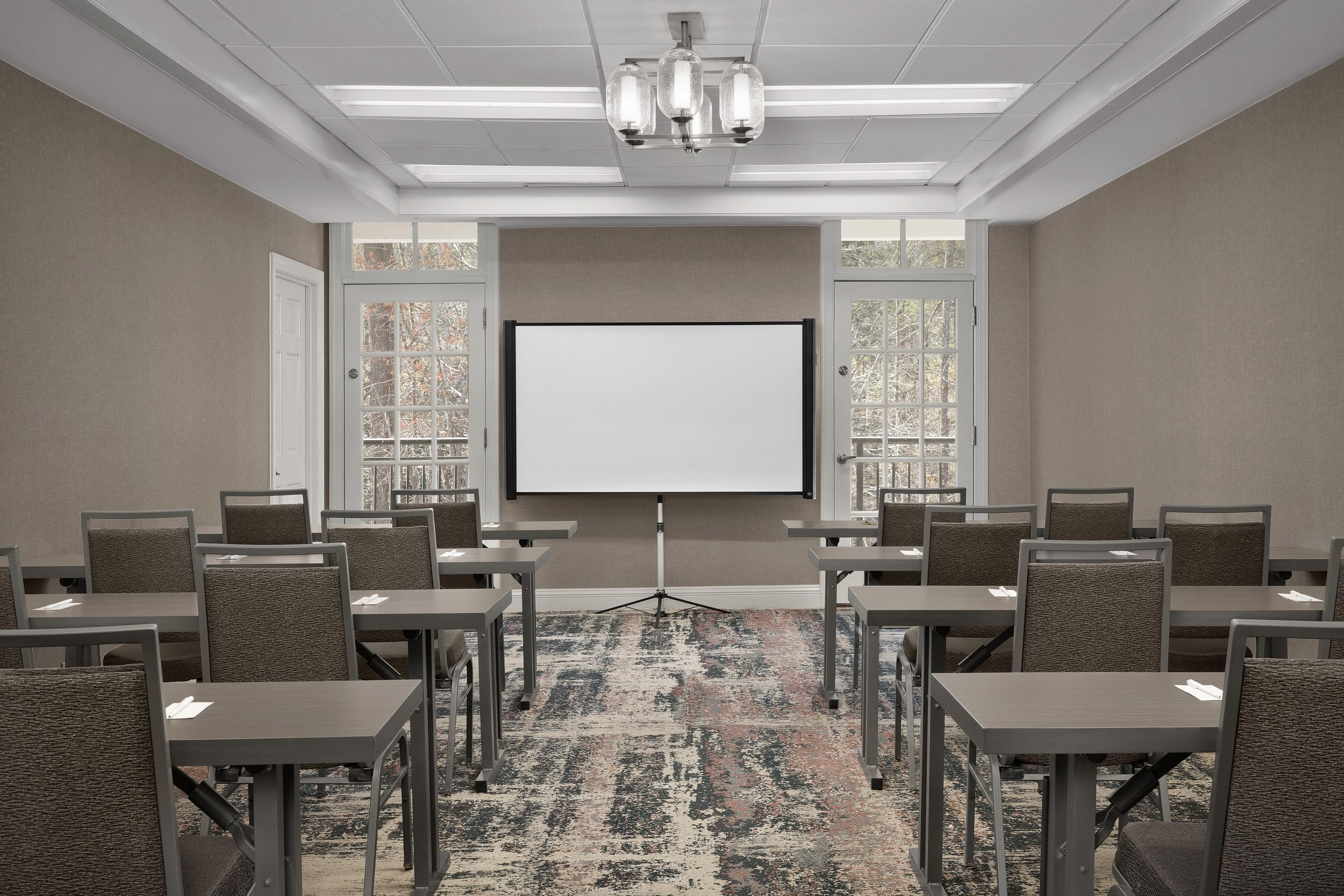 A conference room with a large projection screen, multiple tables, and chairs arranged for meetings.