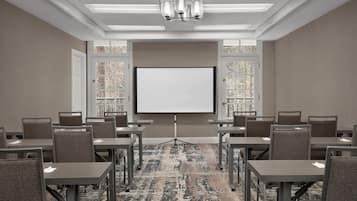 A conference room with a large projection screen, multiple tables, and chairs arranged for meetings.