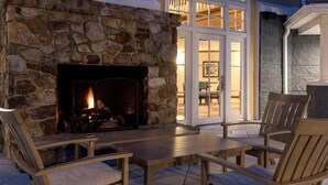 A stone fireplace with a fire, wooden furniture, and a view of a balcony with glass doors.