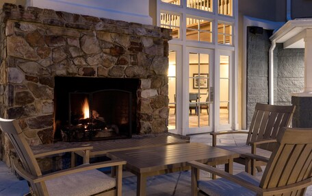 A stone fireplace with a fire, wooden furniture, and a view of a balcony with glass doors.