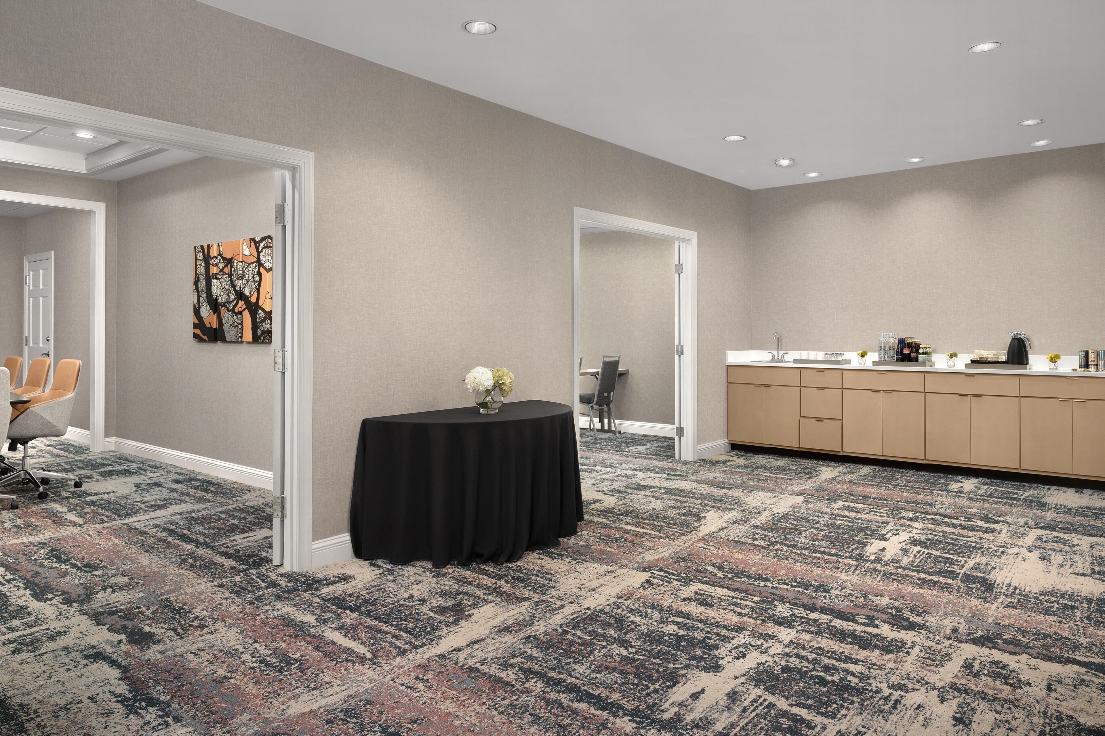 A conference room with a carpeted floor, a round table with a black tablecloth, and a painting on the wall.