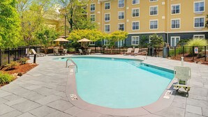 A swimming pool with lounge chairs and umbrellas, surrounded by a fence and trees.