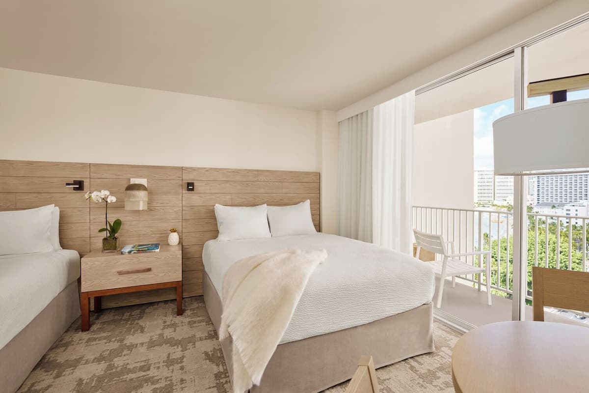 Habitación de hotel con dos camas, un balcón con vistas, una mesita y una silla.
