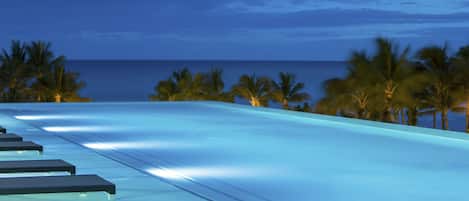 A rooftop pool area with a view of the ocean and palm trees.