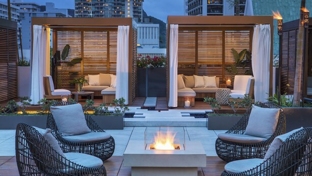Una terraza en la azotea con mobiliario de mimbre, un hogar central y vistas a edificios de la ciudad.