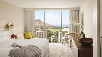 A hotel room with a large bed, a desk, a view of a mountainous landscape, and a dining area.