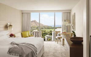 A hotel room with a large bed, a desk, a view of a mountainous landscape, and a dining area.