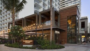Un hotel moderno con bar en la azotea, asientos al aire libre y un cartel que dice "Aloha Hilton Resort".