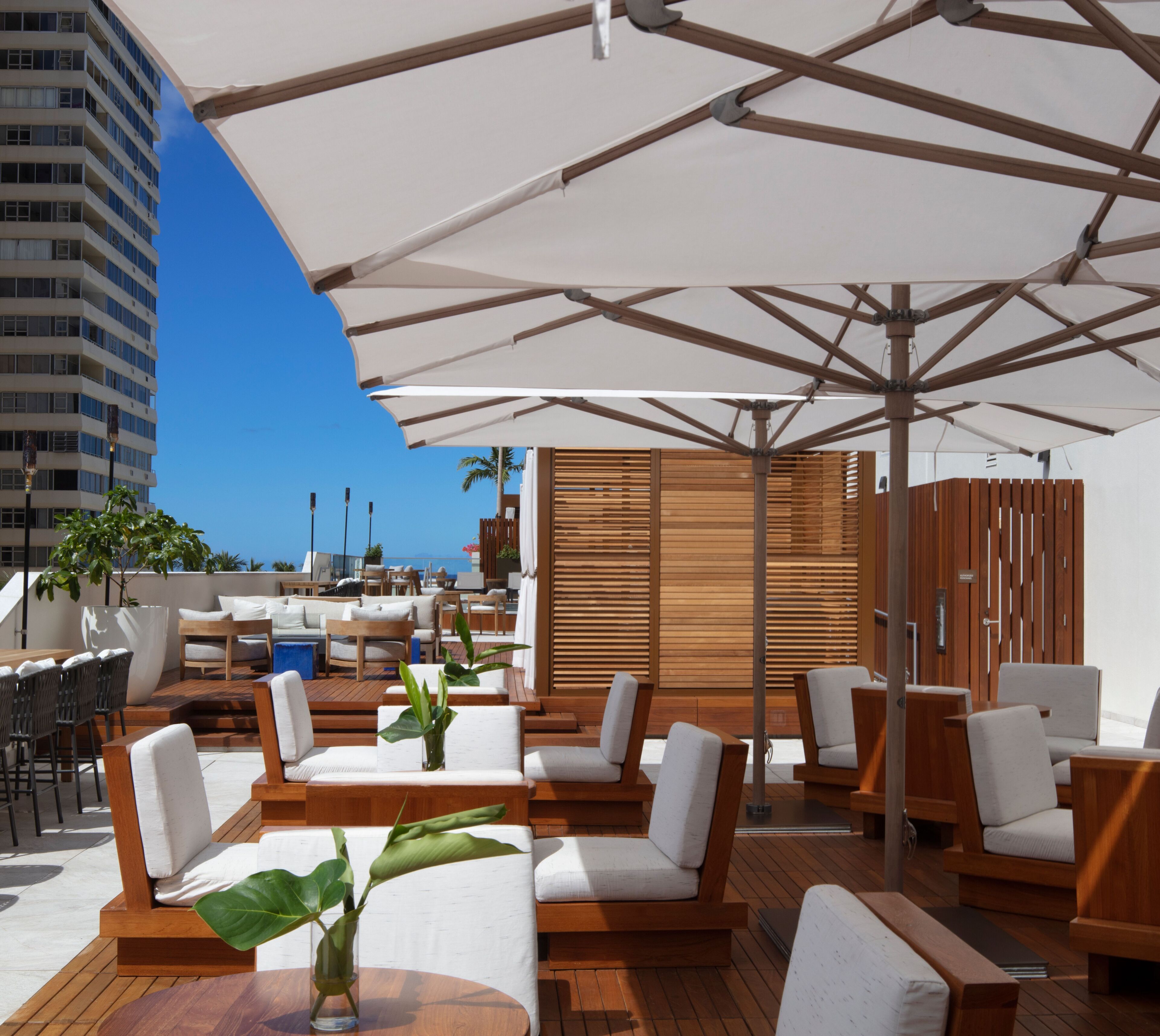 Terraza en la azotea con asientos al aire libre y sombrillas, con vistas a un paisaje urbano.