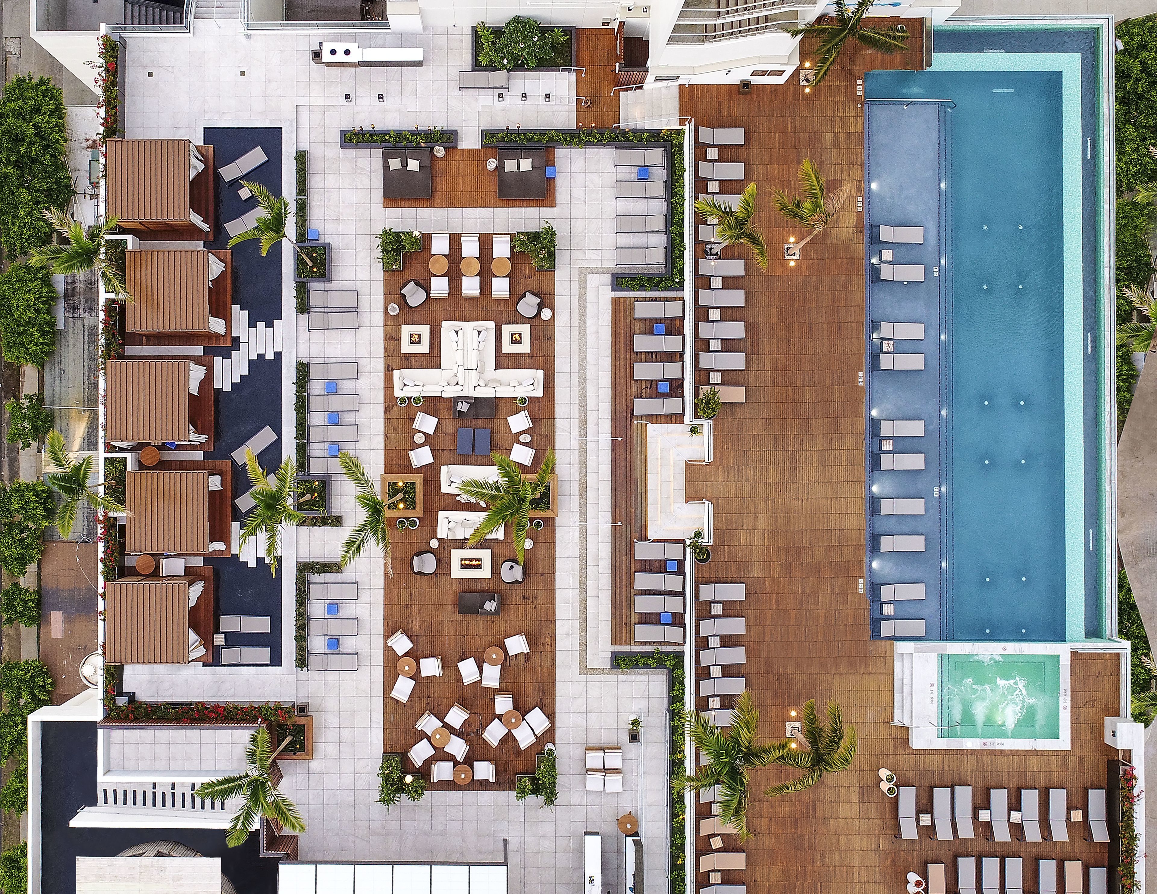 An aerial view of a rooftop pool area with multiple lounge areas, a swimming pool, and surrounding greenery.