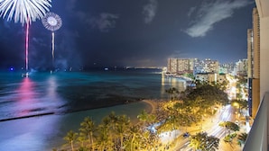 Vista nocturna de un paisaje urbano frente al mar, con edificios iluminados y una playa con palmeras.