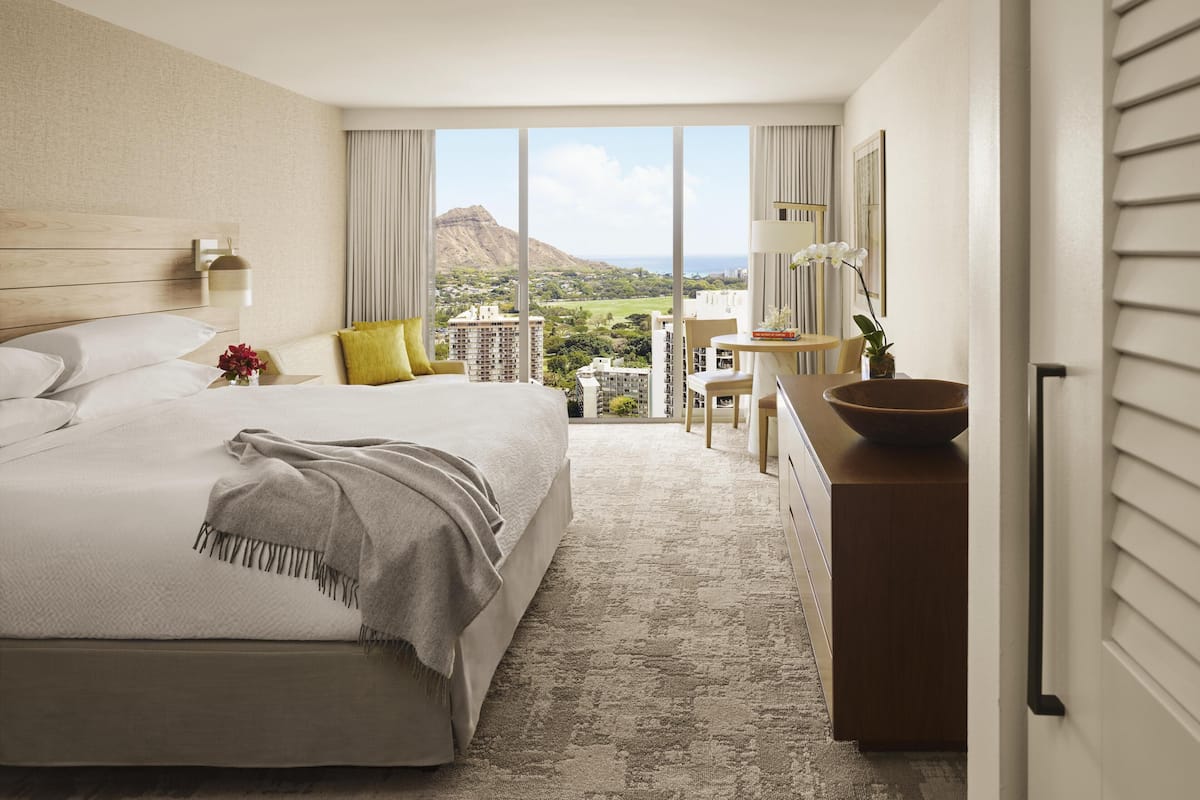 Una habitación de hotel con una cama grande, un escritorio y vistas a la montaña y al paisaje urbano.
