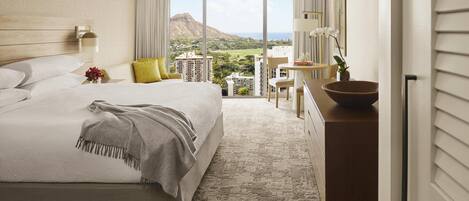 A hotel room with a large bed, a desk, and a view of a mountain and cityscape.