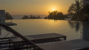A sunset view from a poolside area with lounge chairs and a building in the background.