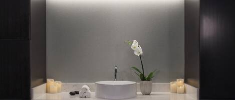 A bathroom with a round white sink, a potted orchid, and candles.