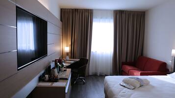 Une chambre d’hôtel avec un lit, un bureau et une chaise, une télévision et un canapé rouge.