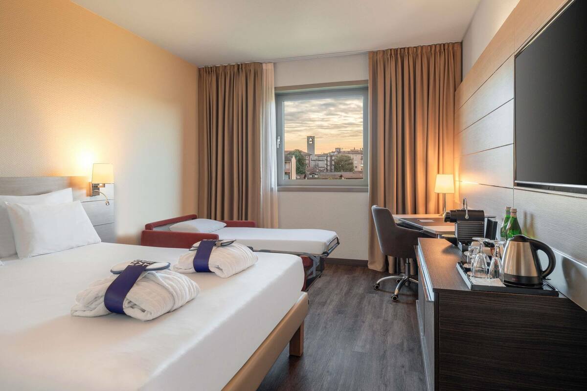 Une chambre d’hôtel avec deux lits, un bureau, une chaise, une machine à café et une fenêtre donnant sur la ville.