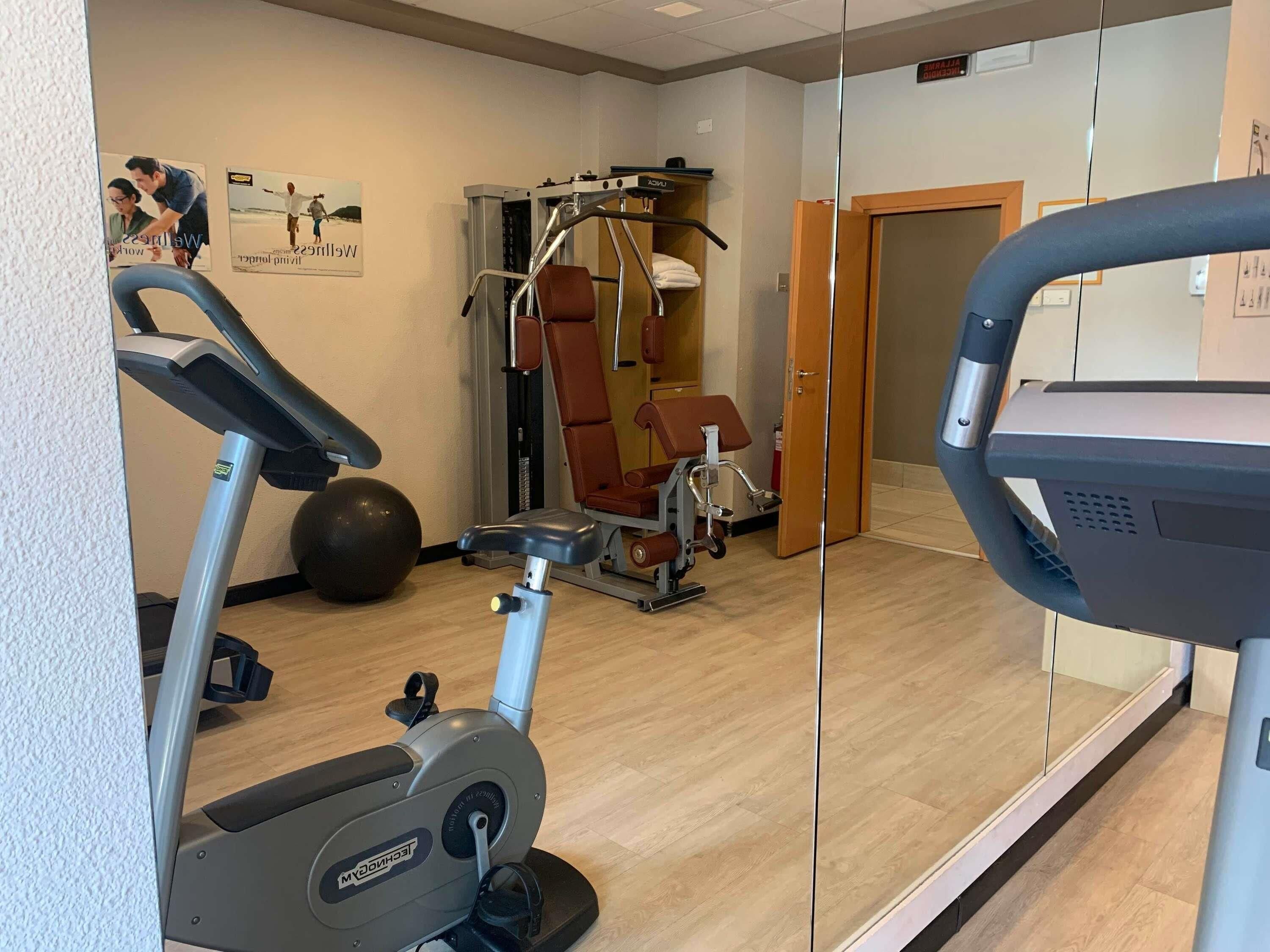 A gym with cardio equipment, weight machines, and a mirrored wall.