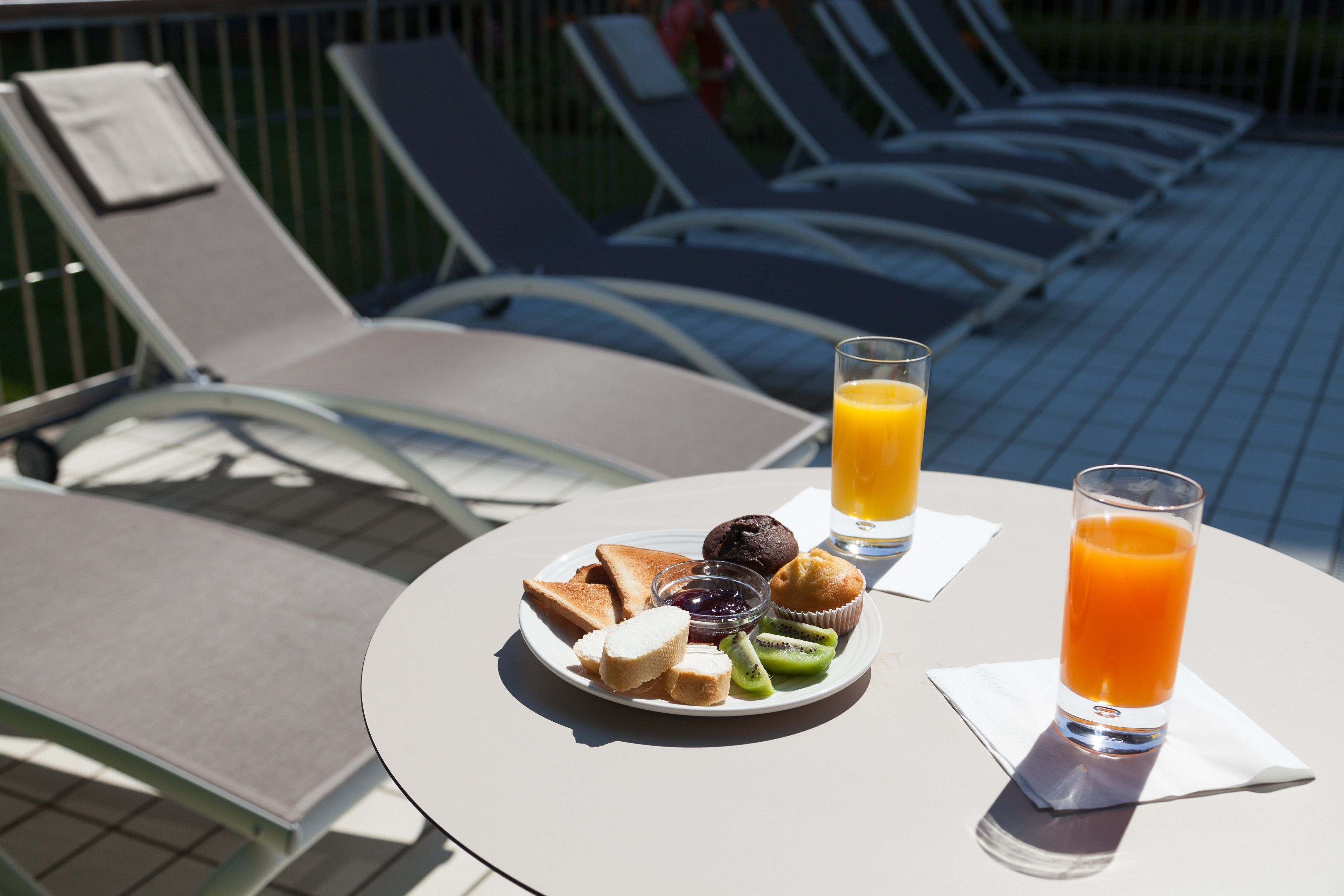 Una mesa de desayuno con tostadas, muffins, kiwi y vasos de jugo.