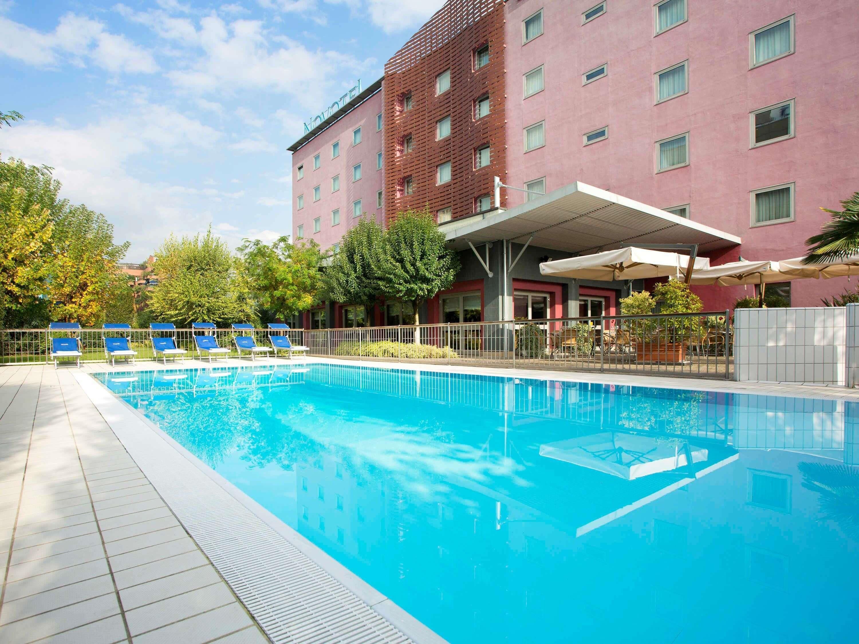 Una piscina con sillones de descanso, una zona de estar cubierta y un edificio con fachada roja y varias ventanas.