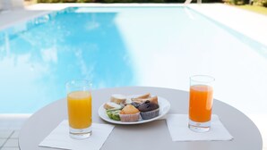 A table with a plate of food and two glasses of orange juice by a pool. - Novotel Brescia 2 (Brescia)