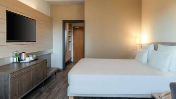Une chambre d’hôtel moderne dotée d’un grand lit, d’un téléviseur à écran plat fixé au mur, d’une commode en bois et d’une table de chevet avec un téléphone.