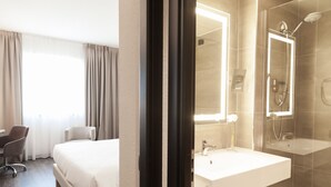 A hotel room with a bed, a desk, a chair, a bathroom with a sink and shower. - Novotel Brescia 2 (Brescia)