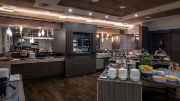 Una cocina de hotel moderna con un sistema de bufé, que incluye una máquina de café, fruteros y una variedad de alimentos.