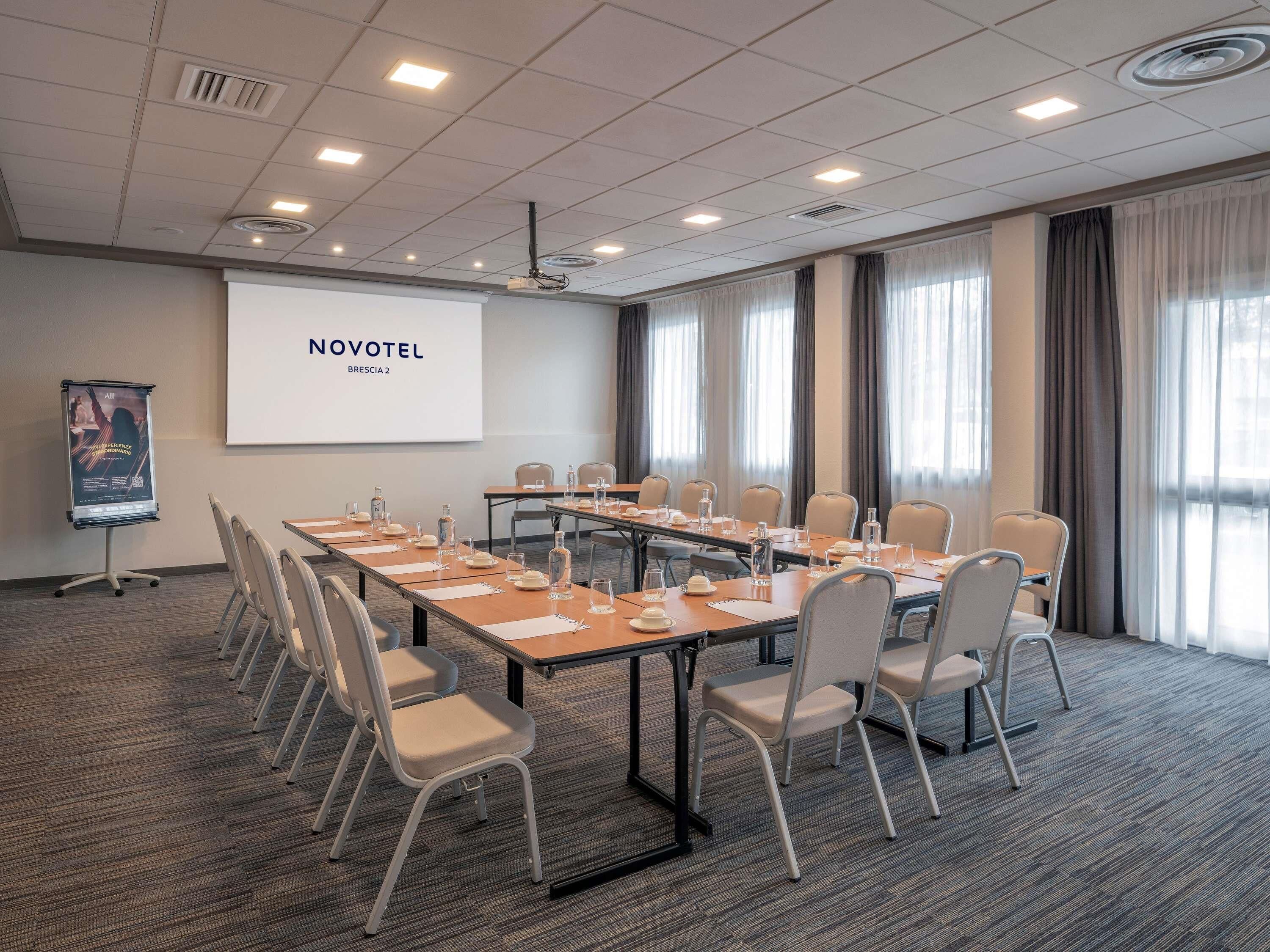 A meeting room with a long table, chairs, a projector screen, and a large window with curtains.