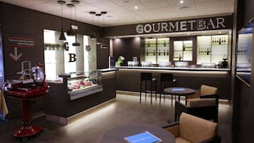 Un bar moderno con un letrero que dice 'GOURMETBAR', una vitrina con productos alimenticios y diferentes disposiciones de asientos.