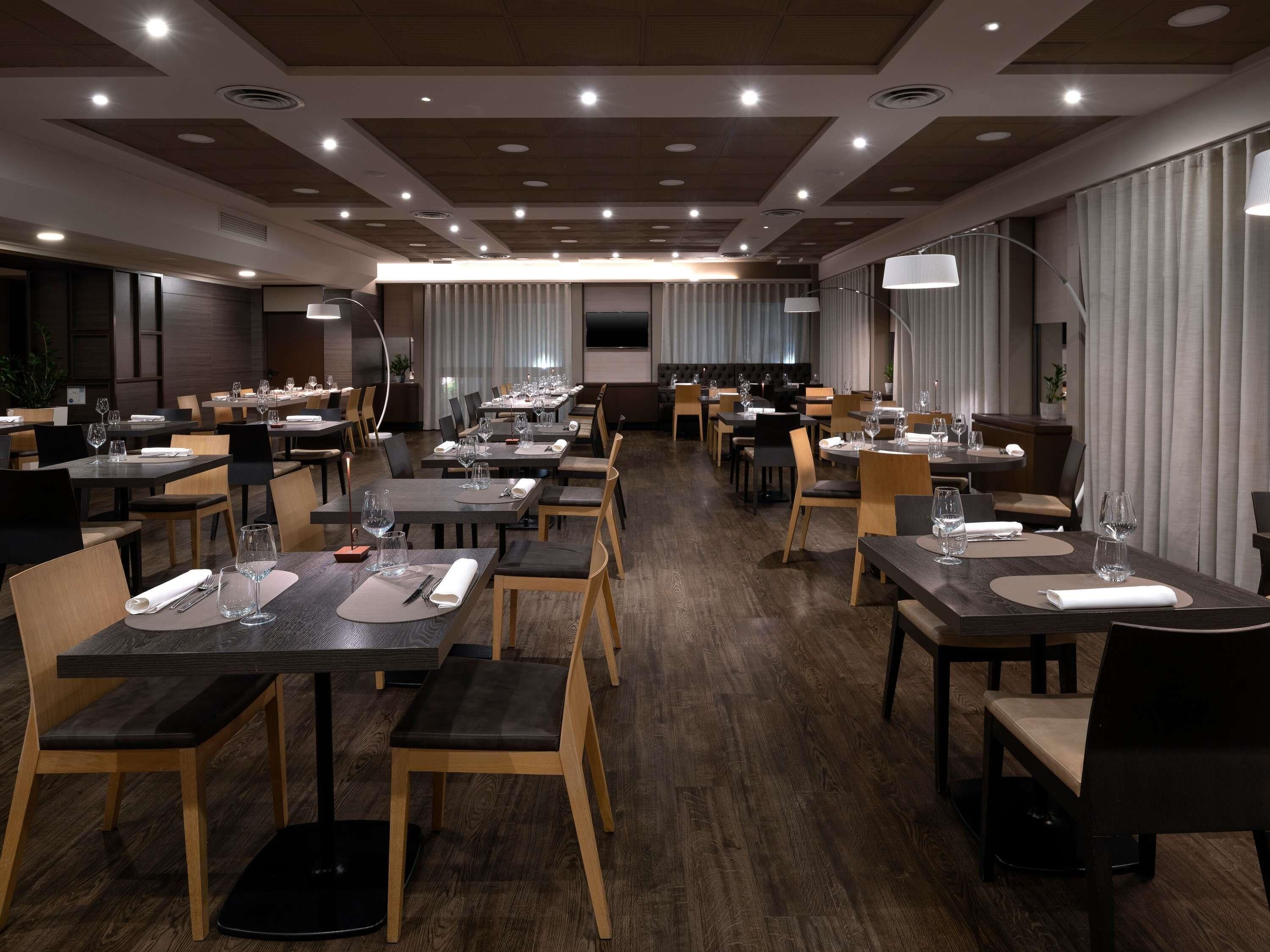 Comedor de hotel con varias mesas, sillas y una pantalla grande.
