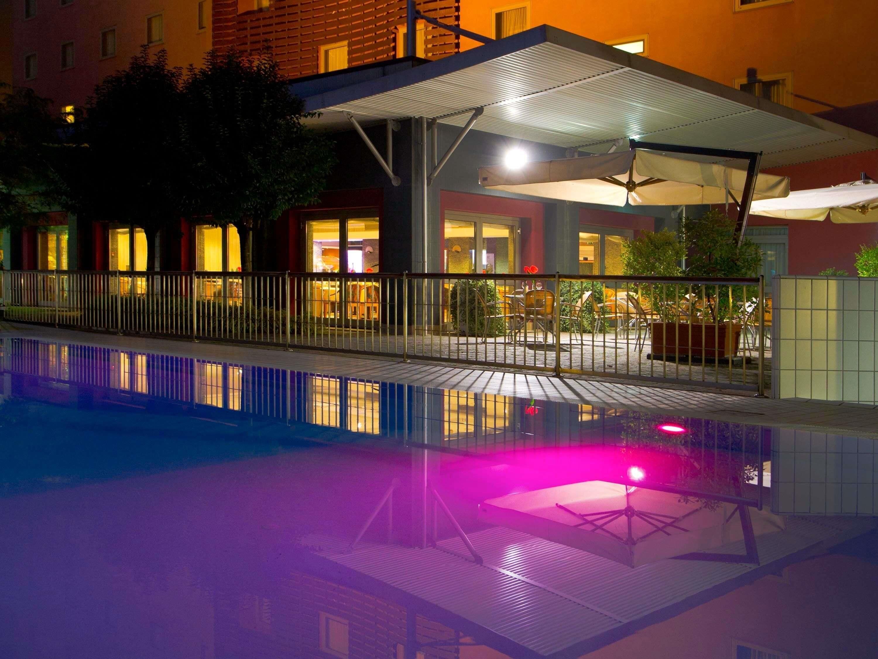 Vista nocturna de un hotel con piscina, zona de estar al aire libre y terraza cubierta.