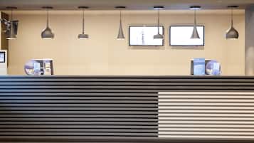 A reception desk with a modern design, featuring a black and white striped pattern, multiple pendant lights, and two flat-screen TVs mounted on the wall.