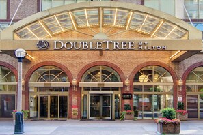 Fachada del hotel DoubleTree by Hilton, con una entrada destacada, ventanas en arco y una cubierta de vidrio.