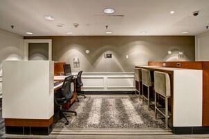 Een vergaderzaal met een lange tafel, stoelen, een spreekgestoelte en een vloerkleed.
