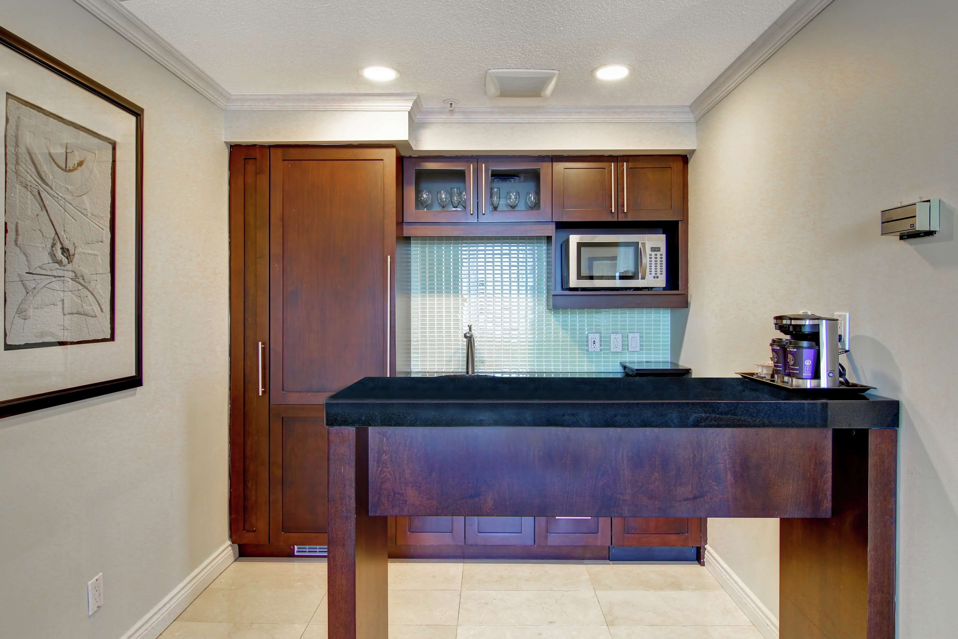 A kitchen with wooden cabinets, a black countertop, a microwave, and a coffee maker.