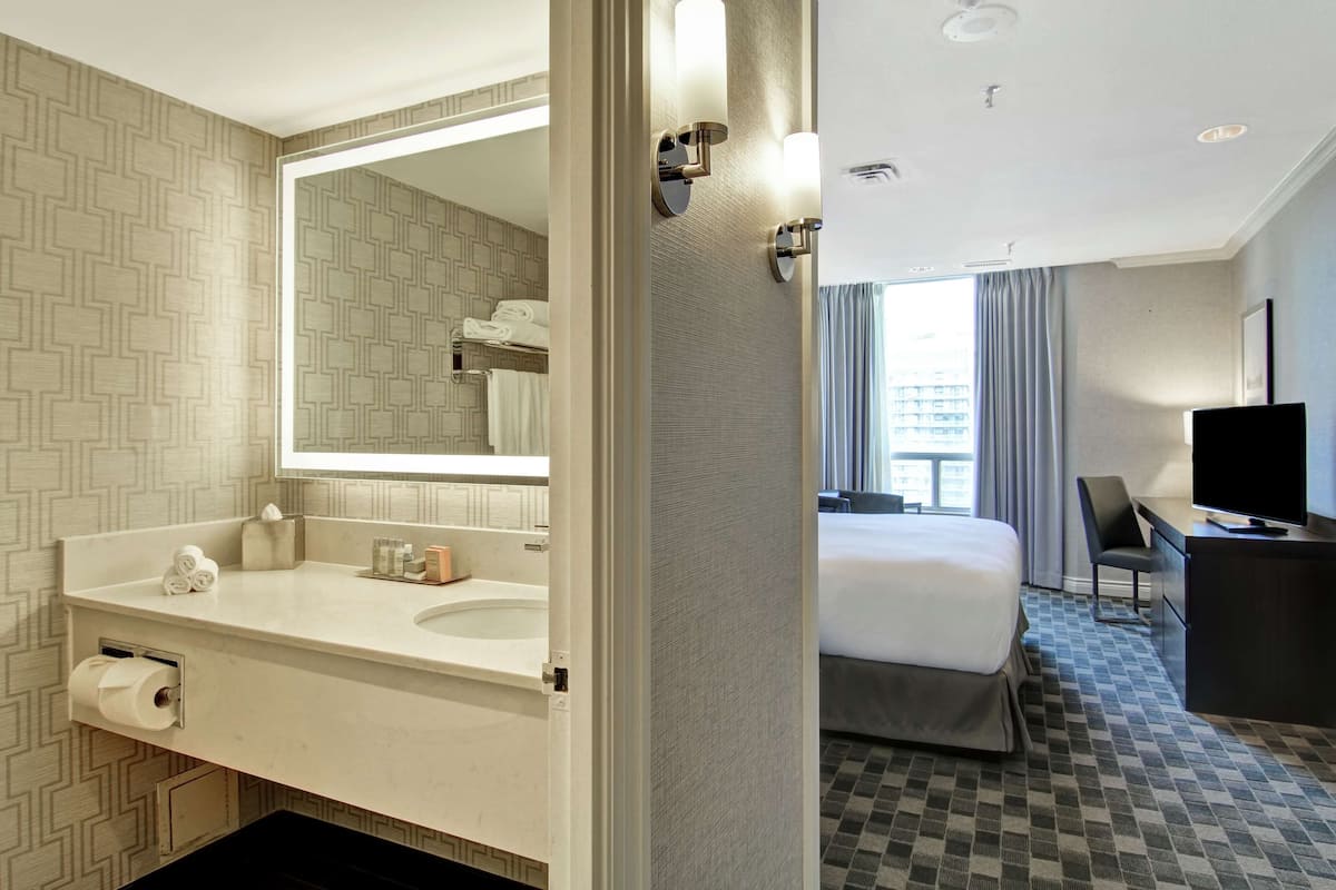 A hotel room with a large mirror, a bed, a desk, and a television.