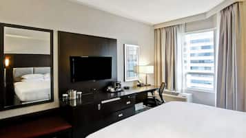 Een hotelkamer met een groot bed, een flatscreen-tv, een bureau met een lamp, een telefoon en een raam met gordijnen.