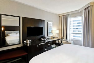 Een hotelkamer met een groot bed, een flatscreen-tv, een bureau met een lamp, een telefoon en een raam met gordijnen.