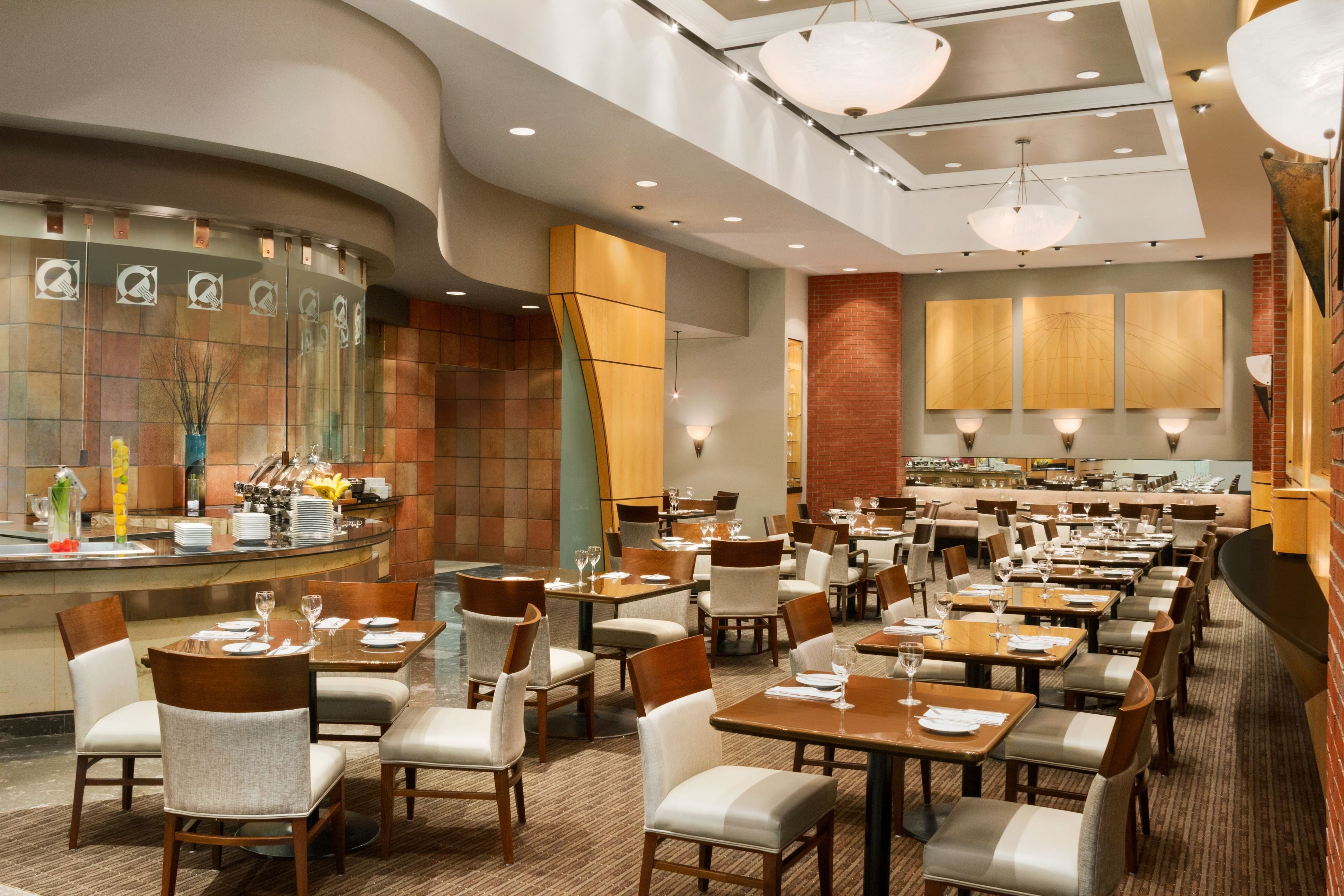 Un restaurant moderne doté d’un bar aux lignes courbes, de plusieurs tables et d’un éclairage contemporain.