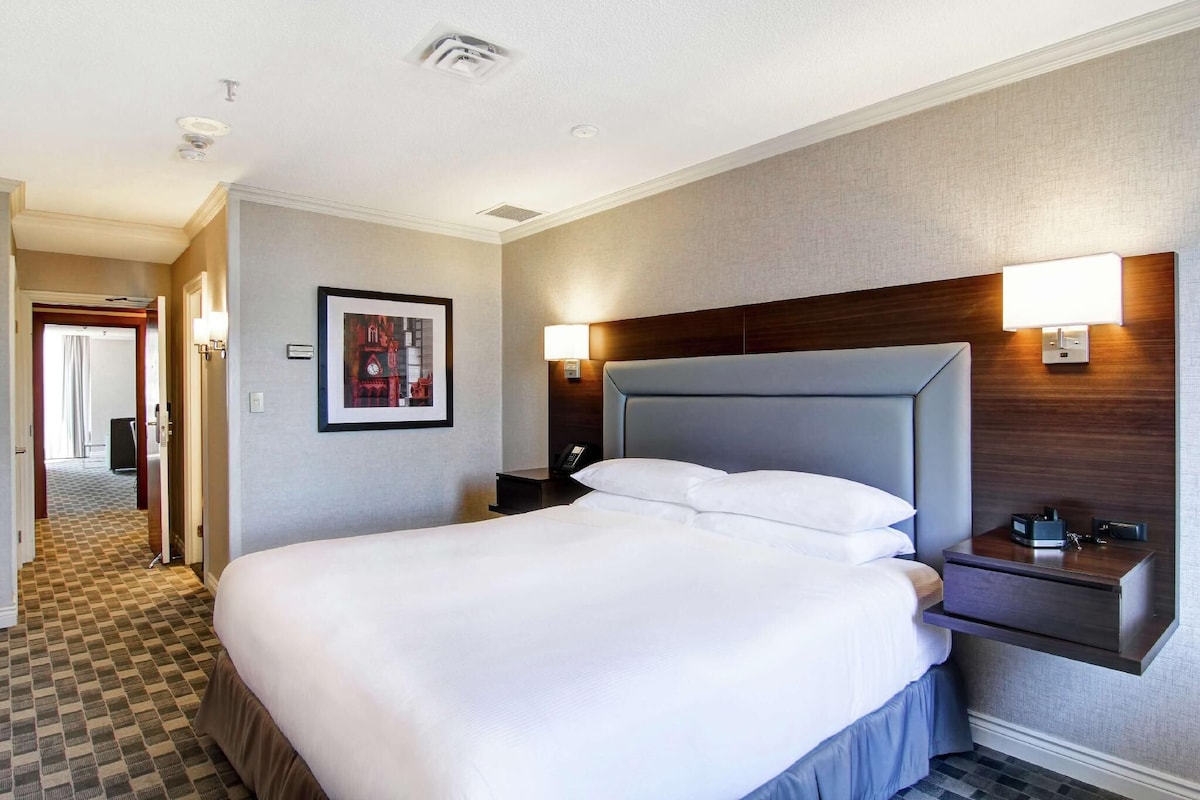 Habitación de hotel con una cama grande, mesitas de noche, cabecero y un cuadro enmarcado en la pared.