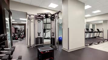 Een fitnessruimte met krachtapparaten, loopbanden en een squats rek.