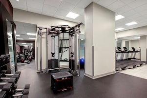 Een fitnessruimte met krachtapparaten, loopbanden en een squats rek.