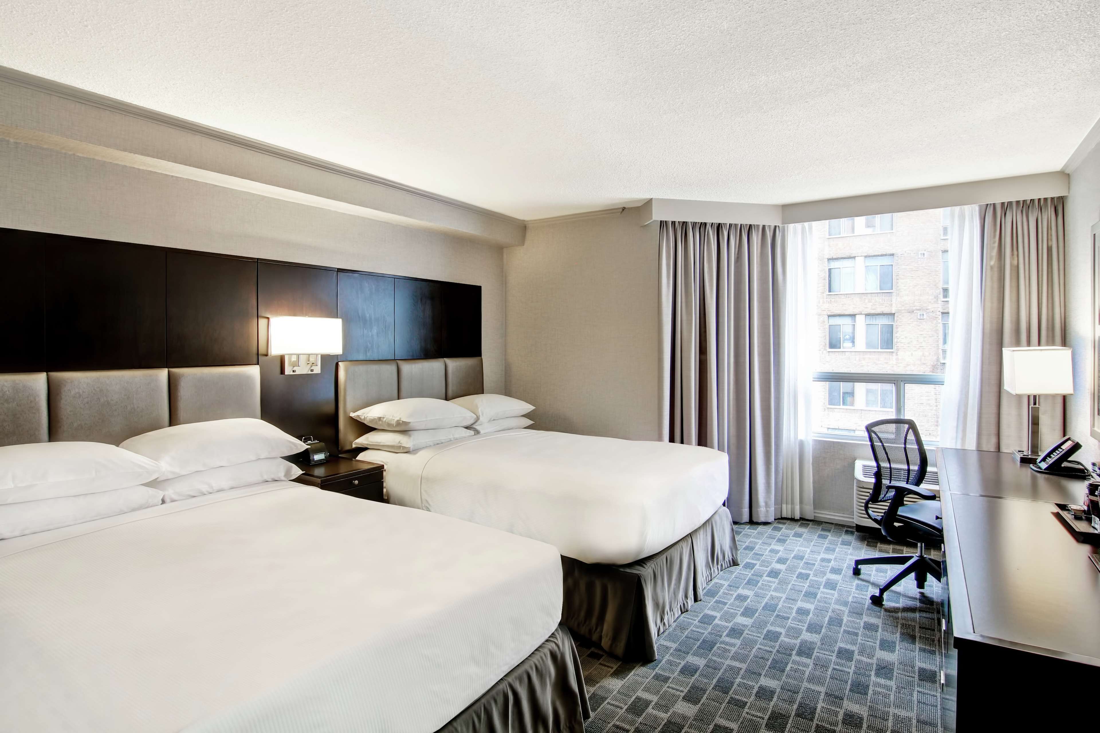 A hotel room with two beds, a desk, a chair, and a window with curtains.
