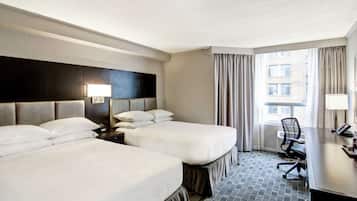 A hotel room with two beds, a desk, a chair, and a window with curtains.