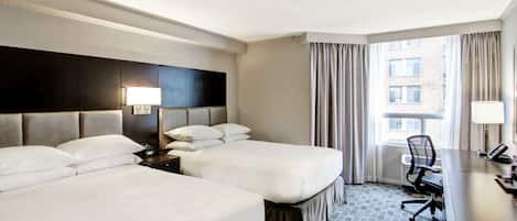Habitación de hotel con dos camas, un escritorio, una silla y una ventana con cortinas.
