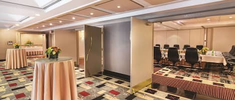 Un salón de conferencias con alfombra estampada, mesas redondas con sillas y un espejo grande en la pared.